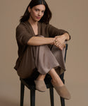Woman sitting on a chair wearing a brown outfit against a beige background