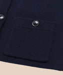 Close-up of the Charlotte Cardigan in navy blue, showing a ribbed front pocket with a round shiny button above it. Another button and part of the placket are visible to the side.