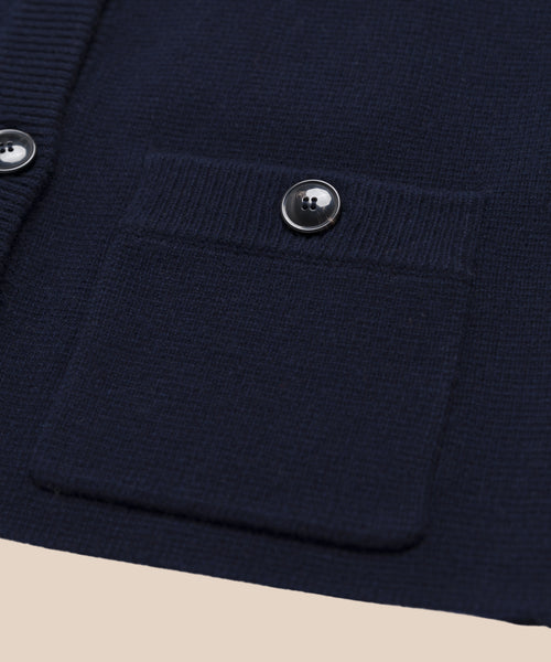 Close-up of the Charlotte Cardigan in navy blue, showing a ribbed front pocket with a round shiny button above it. Another button and part of the placket are visible to the side.