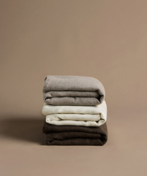 Stack of folded throws in gray, white, and chocolate on a beige background