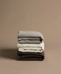 Stack of folded clothes in gray, white, and brown on a beige background