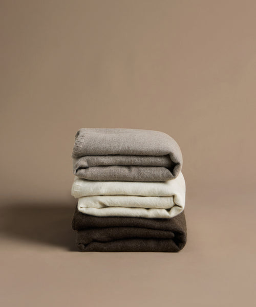 Stack of folded clothes in gray, white, and brown on a beige background