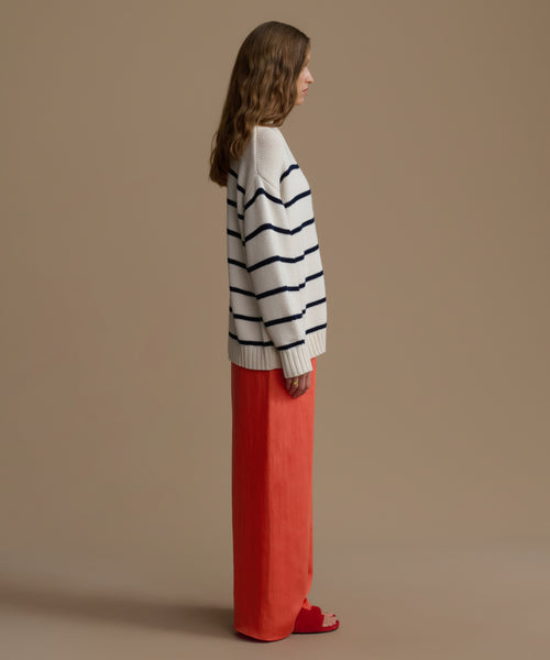 Woman wearing a striped sweater and red pants against a beige background