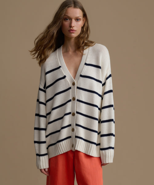 Woman wearing a white cardigan with black stripes and red pants on a beige background