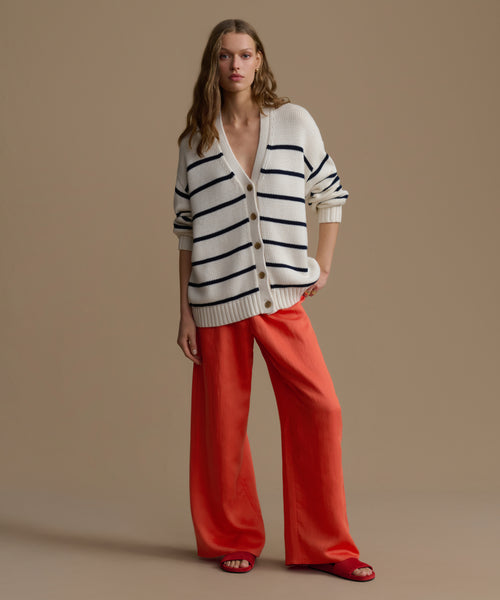 Woman wearing a striped cardigan and red pants against a beige background