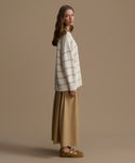 Woman wearing a striped sweater and beige skirt against a brown background