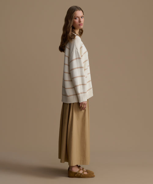 Woman wearing a striped sweater and beige skirt against a brown background