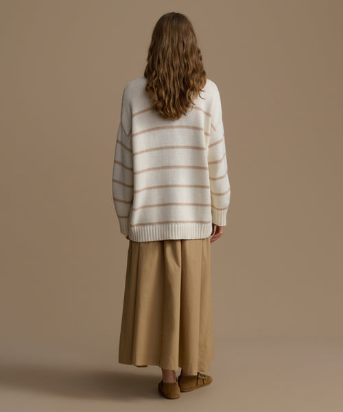 Person wearing a striped sweater and beige pants against a plain background