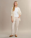 A woman with long blonde hair stands against a beige background wearing the Chloe Cardigan over a white t-shirt, light beige pants, and brown flats—an ideal addition to your spring and summer wardrobe.