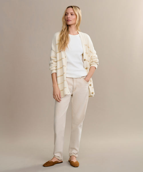 A woman with long blonde hair stands against a beige background wearing the Chloe Cardigan over a white t-shirt, light beige pants, and brown flats—an ideal addition to your spring and summer wardrobe.