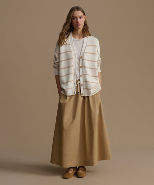 Woman wearing a striped cardigan and beige skirt against a brown background