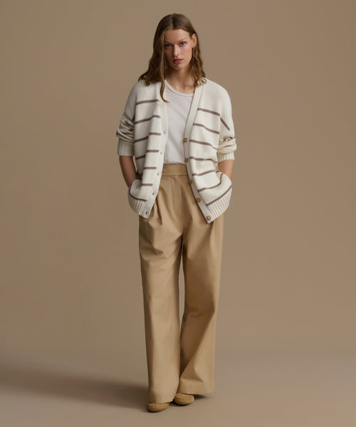 Woman wearing a striped sweater and beige pants against a brown background