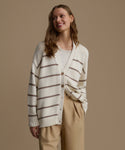 Woman wearing a striped cardigan and beige pants against a brown background