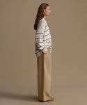 Woman wearing a striped sweater and beige pants against a brown background