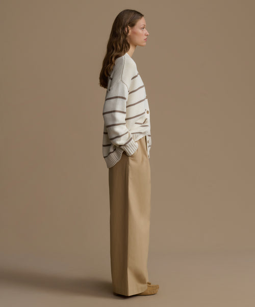 Woman wearing a striped sweater and beige pants against a brown background
