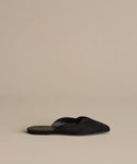 A single Clara Mule in black, featuring a pointed toe and suede finish, is elegantly displayed on a neutral beige background.