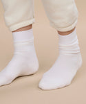 A person stands on a beige surface, wearing off-white sweatpants with rolled cuffs that reveal their feet in Classic Socks, ivory color.