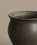 A close-up of the upper half of the Classic Vessel, a matte dark gray handmade vase with a wide round opening and smooth texture, shown against a plain beige background.