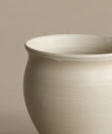 A close-up of the Classic Vessel, an off-white handmade vase featuring a rounded body and slightly flared rim, set against a neutral beige background.