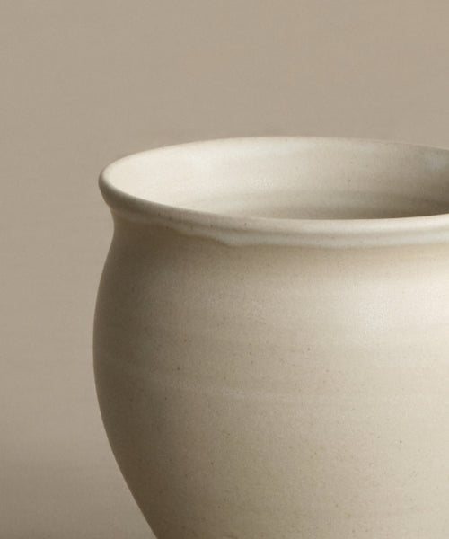 A close-up of the Classic Vessel, an off-white handmade vase featuring a rounded body and slightly flared rim, set against a neutral beige background.