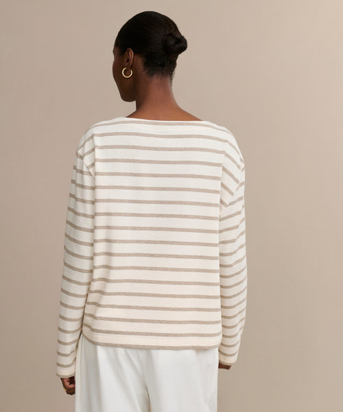 A person with hair in a neat bun wears the Claude Long-Sleeve Tee, featuring nautical stripes, and loose white pants while standing against a plain beige background, shown from the back.