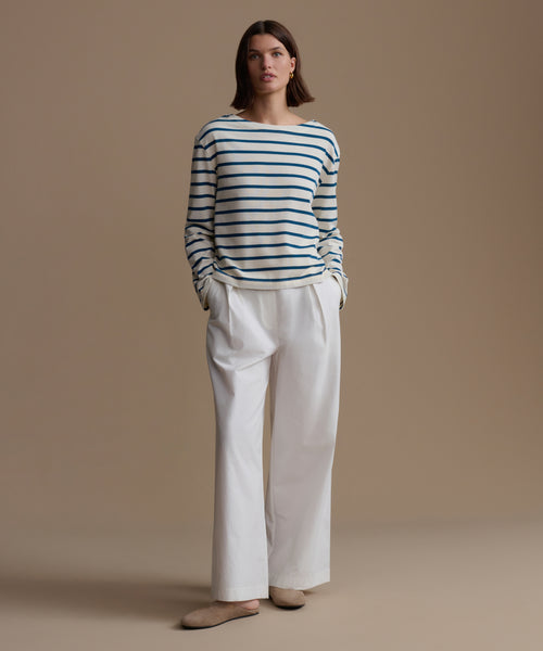 Woman wearing a striped shirt and white pants against a beige background