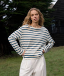 Woman wearing a striped shirt and white pants standing outdoors.