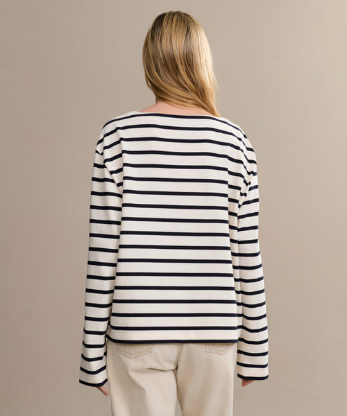 A person with long blonde hair, seen from behind, wears the Claude Long-Sleeve Tee with nautical stripes and light-colored pants against a plain beige background.