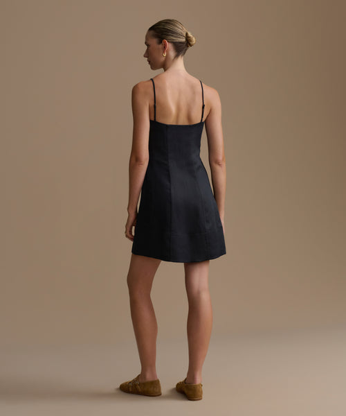 Woman wearing a black Coast dress against a beige background