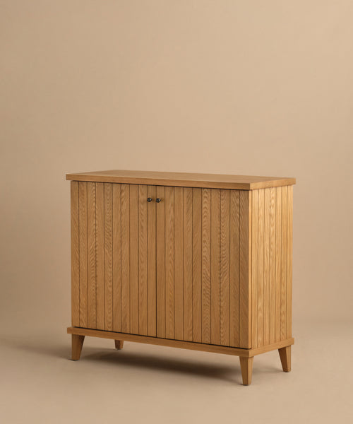 The Coast Hutch is a stylish storage solution featuring vertical slats, two doors, and tapered legs crafted from solid white oak, shown against a plain beige background.