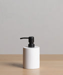 A Coast Soap Dispenser with a black pump, made in Mexico, rests on a light wooden surface in front of a plain light gray background.
