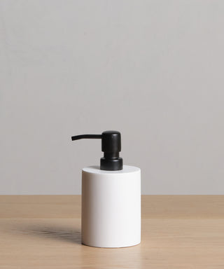 A Coast Soap Dispenser with a black pump, made in Mexico, rests on a light wooden surface in front of a plain light gray background.