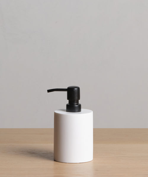 A Coast Soap Dispenser with a black pump, made in Mexico, rests on a light wooden surface in front of a plain light gray background.