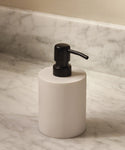 A Coast Soap Dispenser with a black pump rests on a marble bathroom countertop near a backsplash, its handcast resin body lending artisanal style.