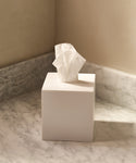 The Coast Tissue Cover, made from handcast resin in white, sits on a marble countertop against neutral walls in the corner of a room, bringing elegant style to your home accessories collection.