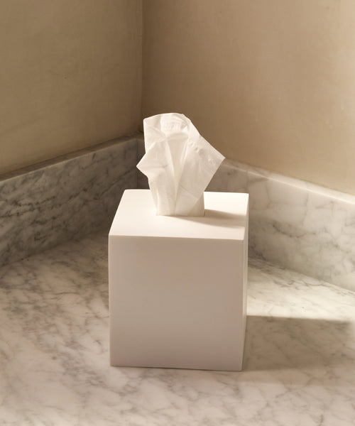 The Coast Tissue Cover, made from handcast resin in white, sits on a marble countertop against neutral walls in the corner of a room, bringing elegant style to your home accessories collection.