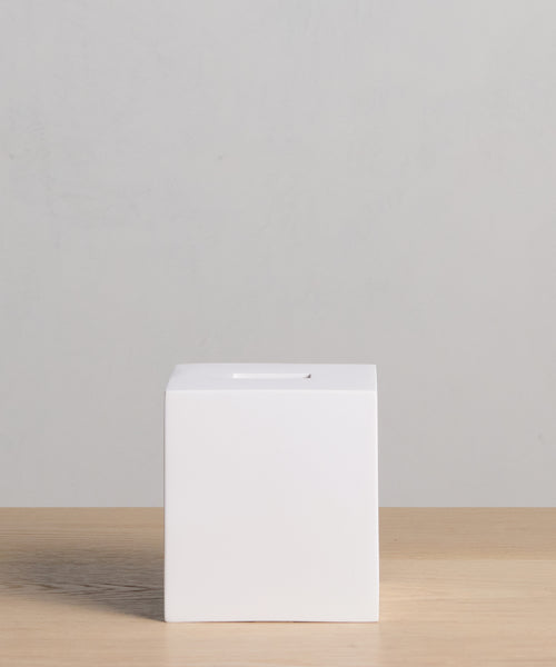 The Coast Tissue Cover, a plain white cube made from handcast resin, rests on a light wood surface with a pale gray backdrop—an elegant accessory for any home.