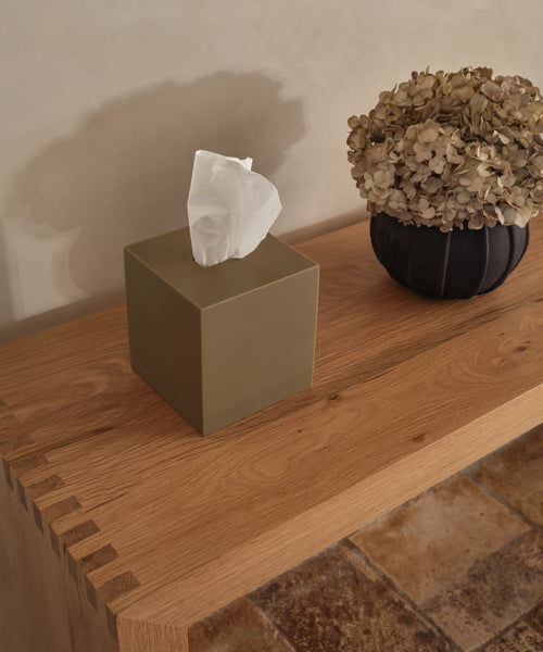 A Coast Tissue Cover in green handcasted resin and a vase of dried hydrangeas sit on a wooden table above a light brown tiled floor—stylish accessories to elevate any space.