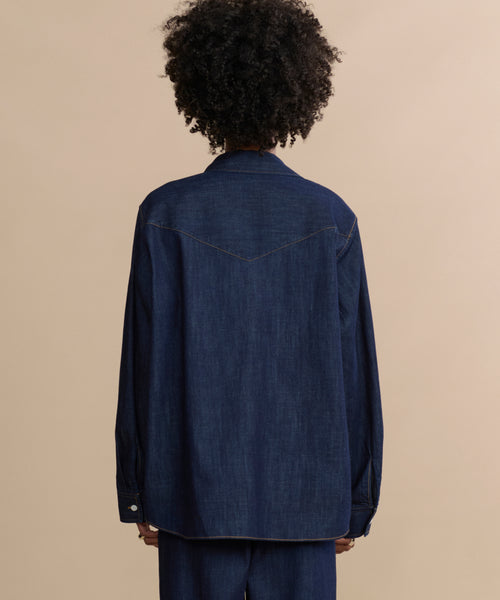 A person with curly hair wears the Colt Shirt—a loose-fitting, long-sleeve Western-inspired top—shown from the back against a beige background, paired with matching pants.