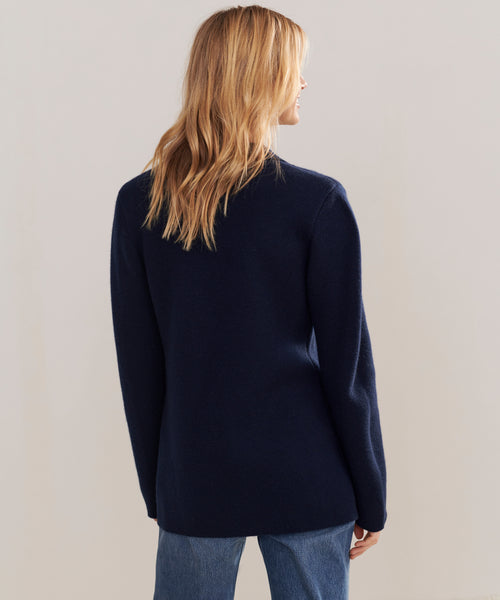 A woman with blonde hair wears the Cooper Blazer in dark navy and blue jeans, standing with her back to the camera against a plain light background.