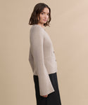 A woman with shoulder-length brown hair wears the Cooper Cardigan, known for its structured silhouette and wide sleeves, paired with a black skirt, standing in profile against a plain beige background.
