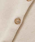 Close-up of the Cooper Cardigan, featuring its cream knit fabric in Warm Ivory and a row of light brown semi-transparent buttons.