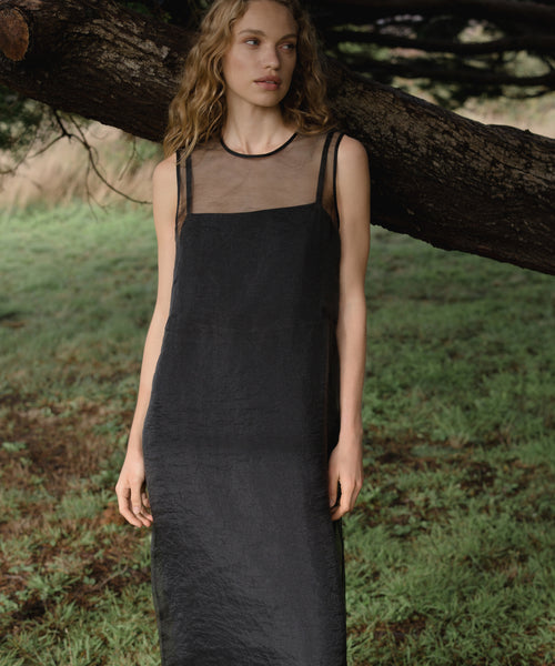 Woman wearing a black cora dress standing under a tree in a natural setting