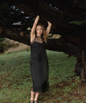 Woman in a black cora dress standing under a large tree in a natural setting