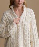 Woman wearing a cream-colored cable knit sweater against a beige background