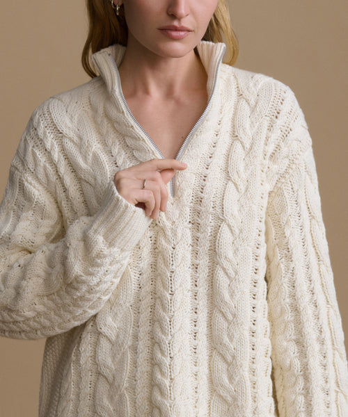 Woman wearing a cream-colored cable knit sweater against a beige background