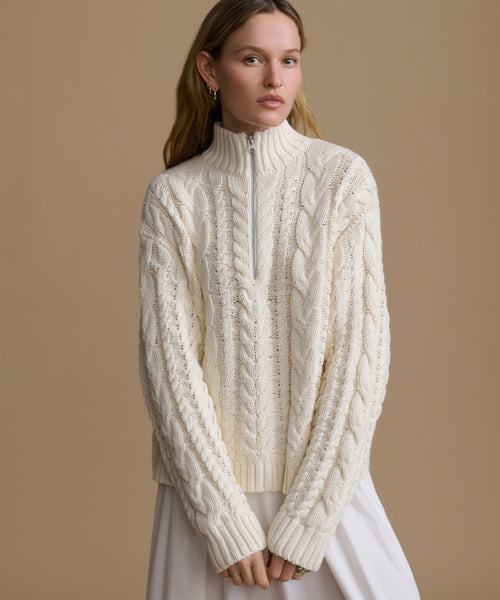 Woman wearing a cream cable knit sweater against a beige background
