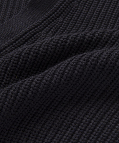 Close-up of the black Cotton Cocoon Cardigan shows ribbed, textured knitted fabric with visible stitches and soft folds, highlighting its detailed woven pattern crafted from organic cotton.