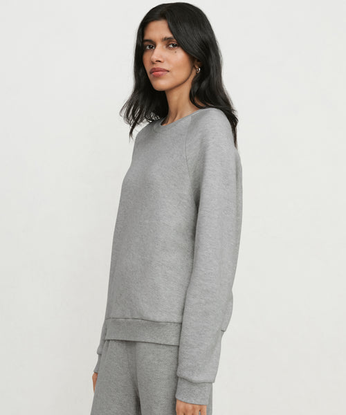 A woman with long dark hair models the Saturday Sweatshirt, made from soft French terry, standing against a plain white background and looking toward the camera with a neutral expression.