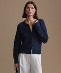 Woman wearing a navy blue cardigan over a white top against a beige background